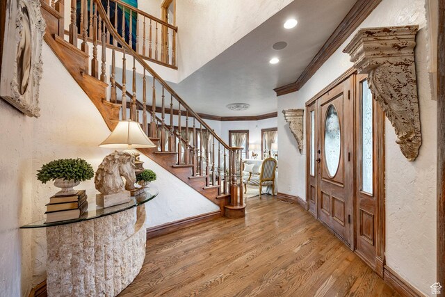 foyer entrance with crown molding, wood finished floors, stairway, baseboards, and a textured wall