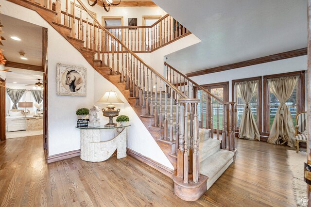 staircase featuring crown molding, ceiling fan, baseboards, wood finished floors, and a towering ceiling