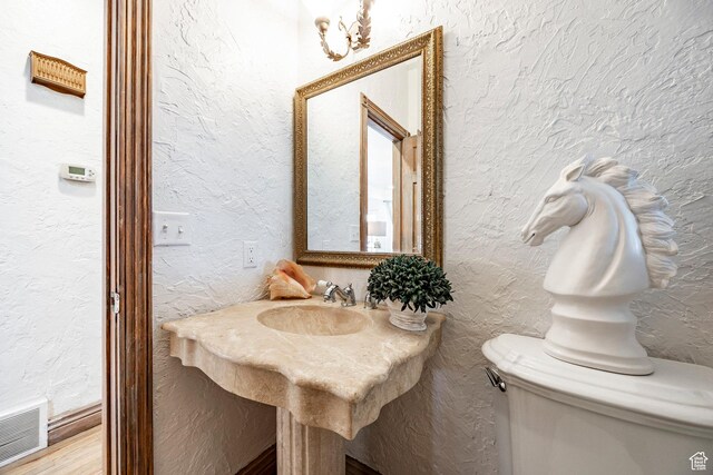 half bathroom with a textured wall, a sink, toilet, wood finished floors, and visible vents