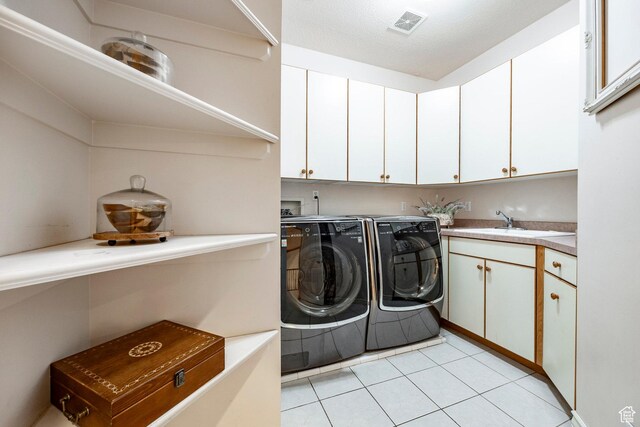 laundry area featuring visible vents, washing machine and clothes dryer, cabinet space, a sink, and light tile patterned floors