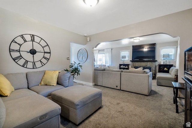 living area featuring arched walkways, a wealth of natural light, a fireplace, and light colored carpet