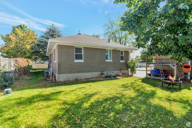rear view of house with brick siding, fence, central AC unit, roof with shingles, and a lawn