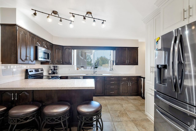 kitchen with a sink, appliances with stainless steel finishes, light countertops, dark brown cabinetry, and a kitchen bar
