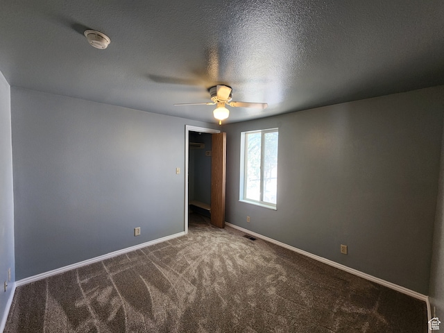 unfurnished bedroom featuring a closet, ceiling fan, a textured ceiling, and dark colored carpet