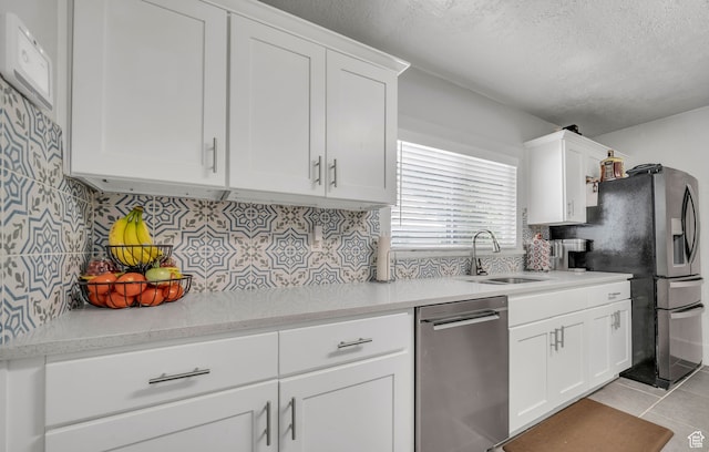 kitchen with stainless steel appliances, sink, light tile patterned floors, white cabinets, and a textured ceiling