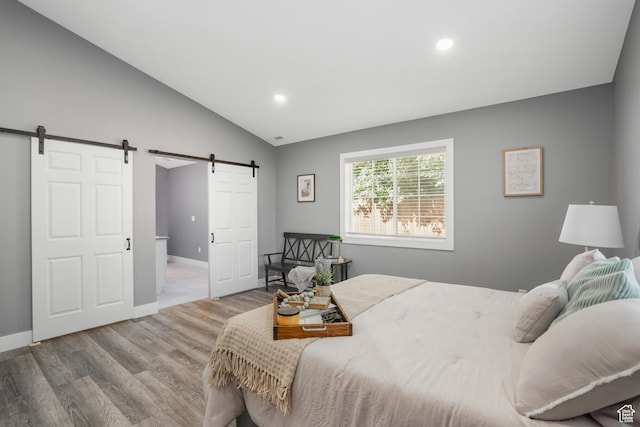 bedroom featuring a barn door, lofted ceiling, wood finished floors, and recessed lighting