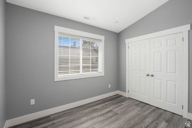 unfurnished bedroom with vaulted ceiling, wood finished floors, a closet, baseboards, and visible vents