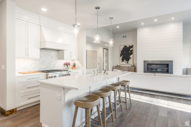 kitchen featuring white cabinetry, custom range hood, a center island with sink, and hanging light fixtures