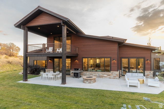 back house at dusk featuring a patio area, a fire pit, a lawn, and a balcony