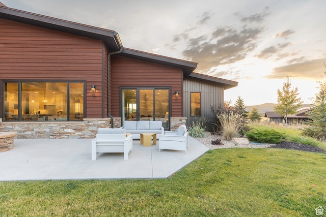 back house at dusk with a patio, a yard, and outdoor lounge area