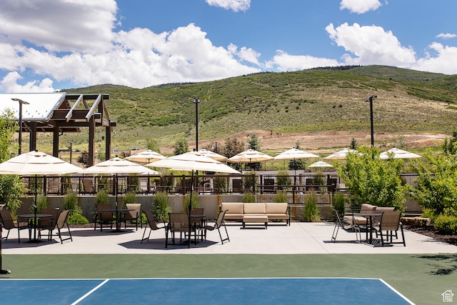 view of tennis court with a mountain view and a patio