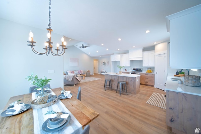 dining room with sink, vaulted ceiling, ceiling fan with notable chandelier, and light hardwood / wood-style floors