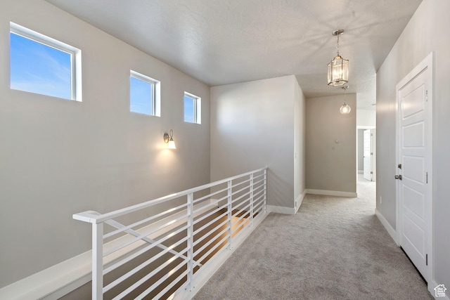 corridor with a notable chandelier, baseboards, carpet flooring, and an upstairs landing
