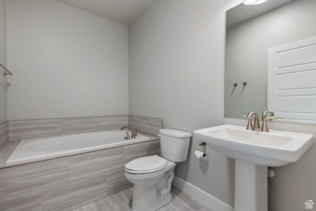 bathroom with a bath, baseboards, a sink, and toilet