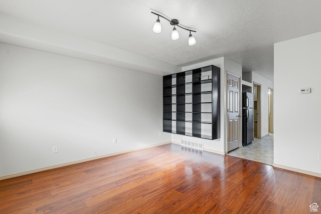 spare room featuring baseboards, visible vents, wood finished floors, and a textured ceiling