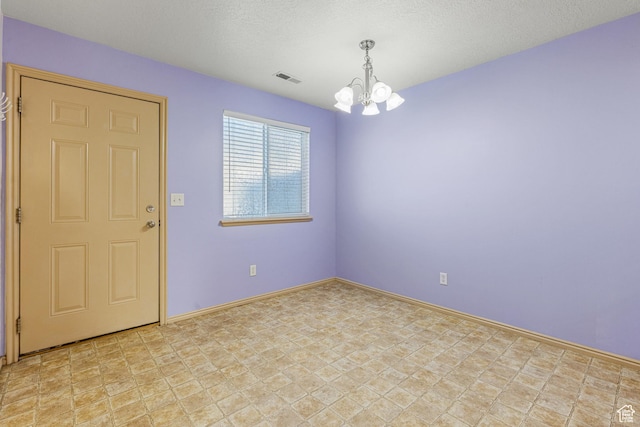spare room with a notable chandelier, a textured ceiling, baseboards, and visible vents