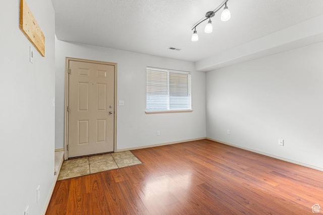 foyer with rail lighting, baseboards, a textured ceiling, visible vents, and wood finished floors