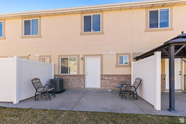 rear view of property featuring stucco siding, fence, a patio, a gazebo, and brick siding
