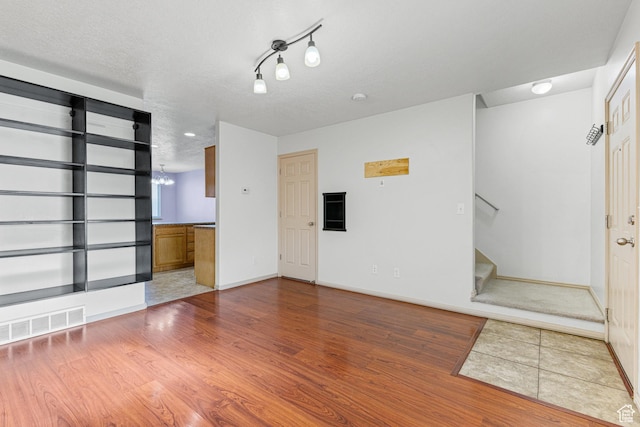 spare room with a textured ceiling, visible vents, baseboards, wood finished floors, and stairway