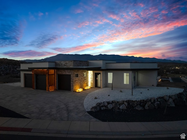 734 S 1220 W, Hurricane, UT 84737 - back of property at dusk with a garage, stone siding, decorative driveway, stucco siding, and a mountain view