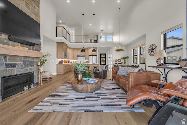 living area with a towering ceiling, recessed lighting, a stone fireplace, and light wood-style floors