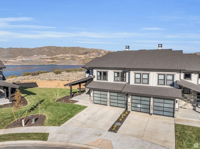 view of front of house with driveway, a shingled roof, a front yard, an attached garage, and a water and mountain view