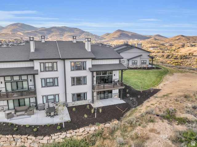 back of property featuring a patio area, a chimney, outdoor lounge area, a mountain view, and roof with shingles