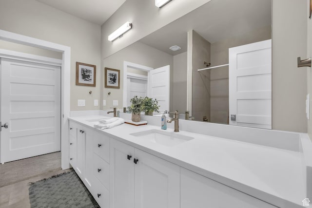 bathroom featuring wood finished floors, a tile shower, double vanity, and a sink