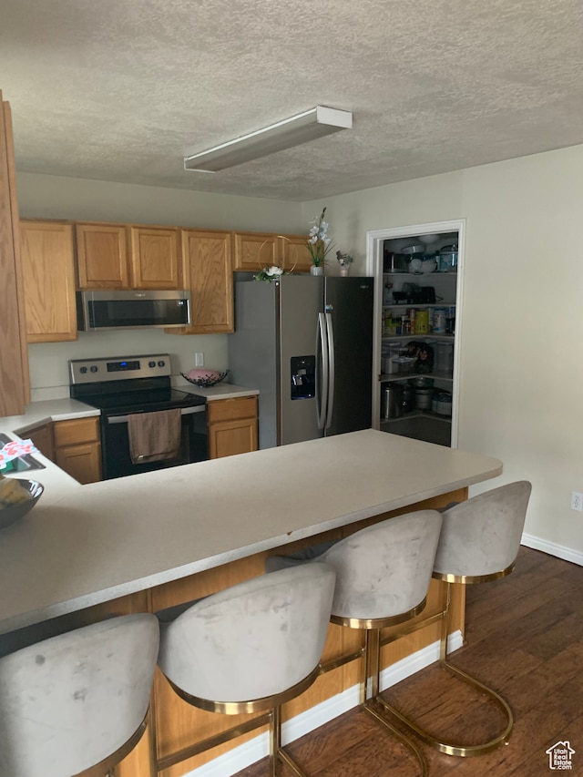 kitchen featuring a textured ceiling, appliances with stainless steel finishes, dark hardwood / wood-style flooring, and kitchen peninsula