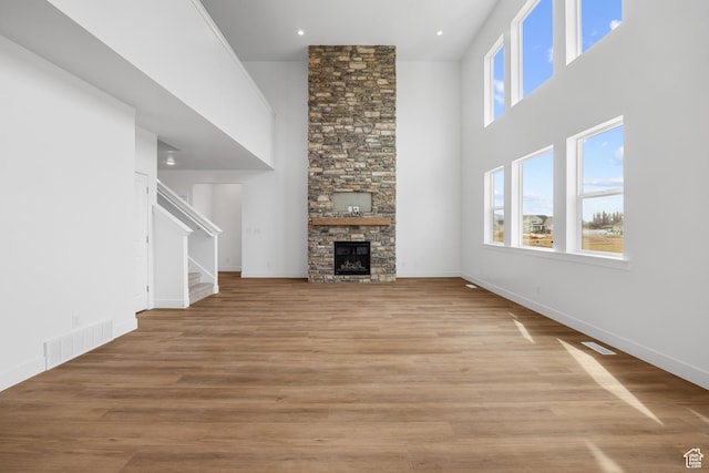 unfurnished living room with a high ceiling, a fireplace, stairs, wood finished floors, and visible vents
