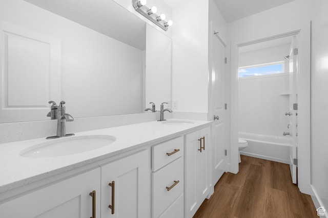 bathroom featuring double vanity, toilet, a sink, and wood finished floors