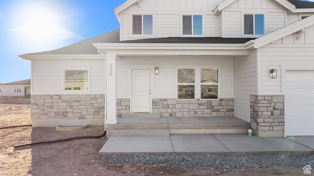property entrance featuring board and batten siding, a shingled roof, stone siding, and a garage