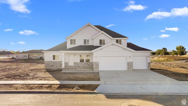 modern farmhouse with a garage, covered porch, stone siding, board and batten siding, and driveway