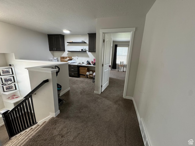 hallway with dark carpet, baseboards, an upstairs landing, and a textured ceiling