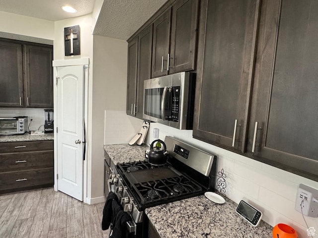 kitchen featuring decorative backsplash, dark brown cabinetry, light stone countertops, and stainless steel appliances