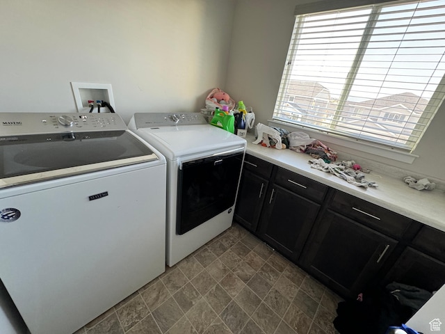 clothes washing area with washing machine and clothes dryer, cabinet space, stone finish floor, and plenty of natural light