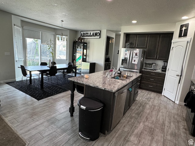 kitchen with a sink, a textured ceiling, a chandelier, light wood-style flooring, and appliances with stainless steel finishes