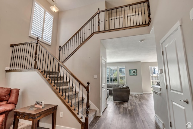 stairway featuring visible vents, baseboards, wood finished floors, and a towering ceiling