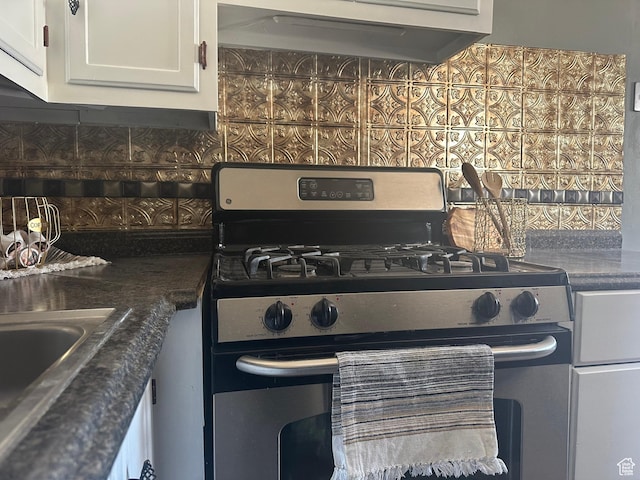 kitchen featuring under cabinet range hood, stainless steel gas stove, white cabinets, and tasteful backsplash