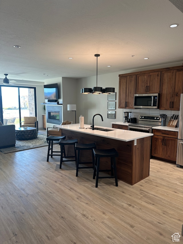 kitchen with a kitchen island with sink, sink, pendant lighting, appliances with stainless steel finishes, and light hardwood / wood-style floors