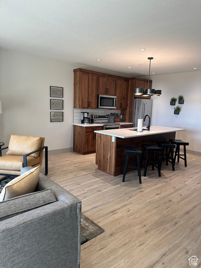 kitchen with a kitchen island with sink, a kitchen bar, light wood-type flooring, pendant lighting, and stainless steel appliances
