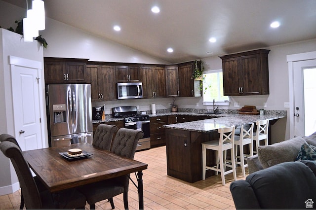kitchen featuring dark brown cabinetry, a peninsula, stainless steel appliances, a sink, and open floor plan