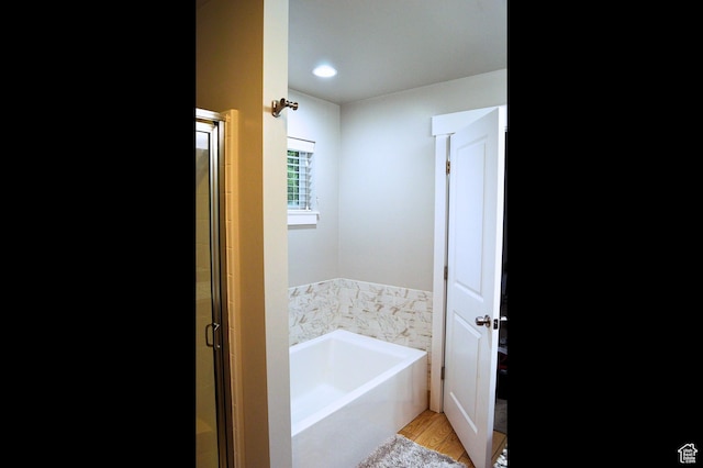 full bath featuring wood finished floors, a garden tub, and a stall shower