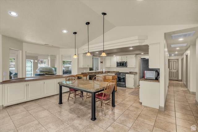 kitchen featuring light tile patterned flooring, kitchen peninsula, stainless steel appliances, lofted ceiling, and white cabinets