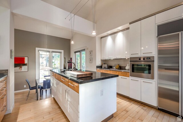 671 N Freeze Creek Cir, Emigration Canyon, UT 84108 - kitchen featuring stainless steel appliances, light wood-style flooring, white cabinets, and a high ceiling