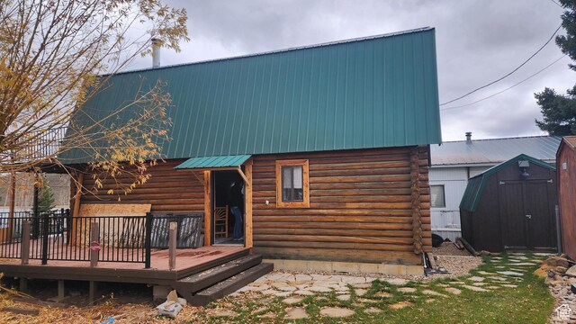 rear view of property featuring metal roof, a deck, an outbuilding, log siding, and a shed