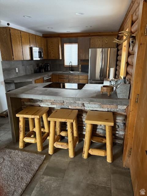kitchen featuring brown cabinets, appliances with stainless steel finishes, decorative backsplash, and a sink