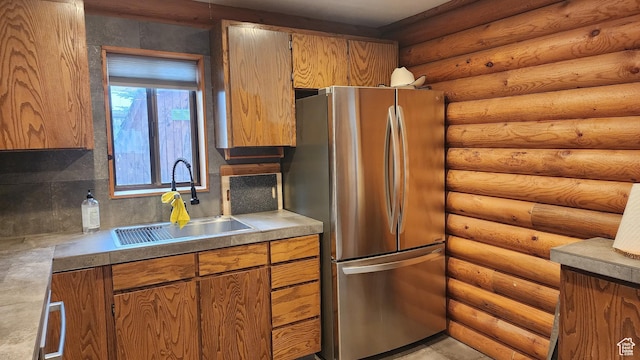 kitchen with brown cabinets, a sink, freestanding refrigerator, backsplash, and log walls