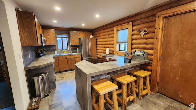kitchen featuring a sink, light countertops, brown cabinetry, stainless steel appliances, and rustic walls