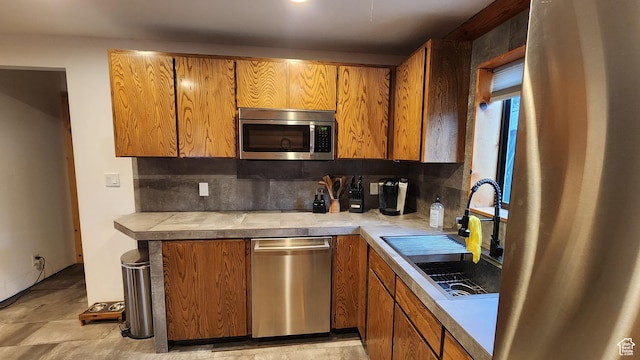 kitchen featuring backsplash, appliances with stainless steel finishes, brown cabinetry, and a sink
